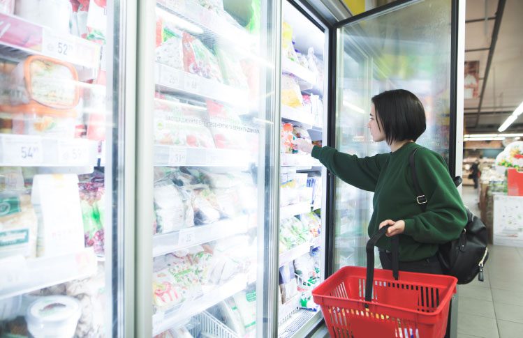 A woman shopping at a grocery store taking frozen food out of a cooler